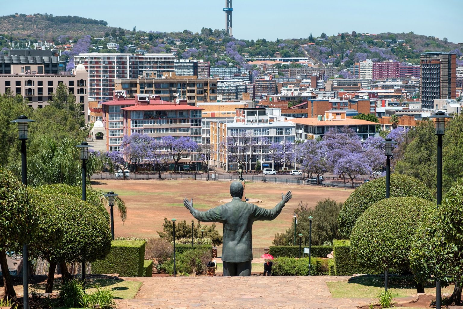 Nelson Mandela statue rear view and the Union Buildings garden, Pretoria, South Africa. Blooming jacaranda trees at background/rawf8/Envato