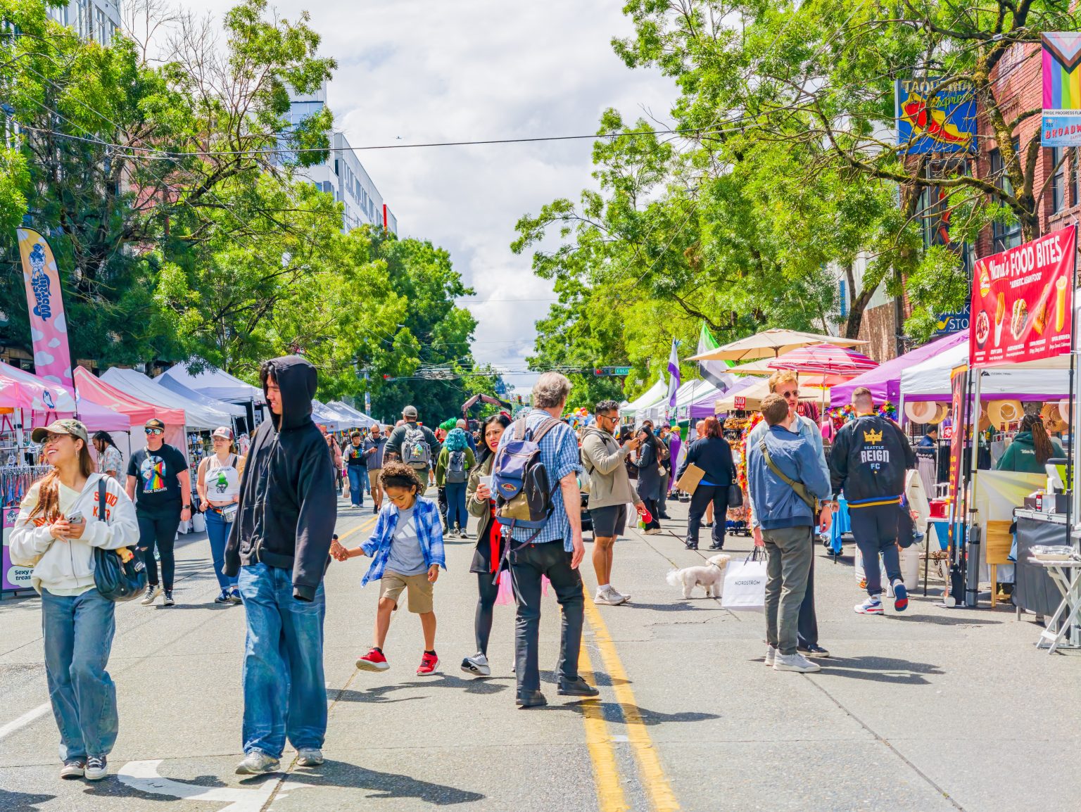 Washington state, United States, JUN 27, 2026 - Diverse group of people walking down a city street lined with vendor tents and colorful umbrellas during a sunny day / Kit Leong / Shutterstock