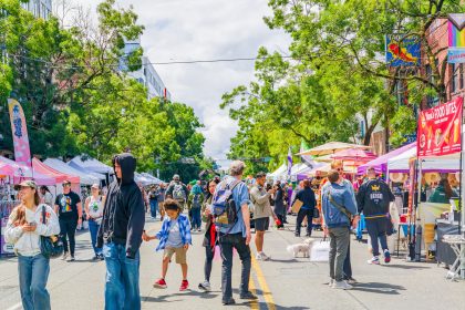 Washington state, United States, JUN 27, 2026 - Diverse group of people walking down a city street lined with vendor tents and colorful umbrellas during a sunny day / Kit Leong / Shutterstock