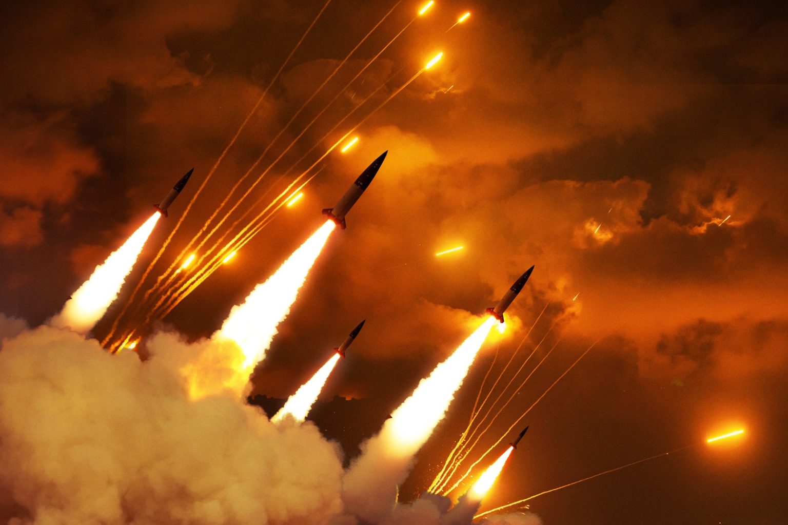Dramatic night scene of a massive ballistic missile strike. Multiple rockets ascending through thick smoke and fire into a glowing orange sky. Concept of Middle East conflict, war, and escalation/Alones/Shutterstock